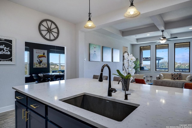 kitchen featuring pendant lighting, light stone countertops, open floor plan, and a sink