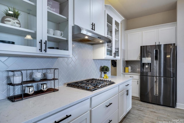 kitchen with white cabinets, light stone countertops, under cabinet range hood, and black fridge