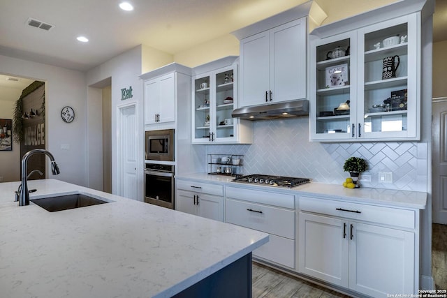 kitchen featuring visible vents, under cabinet range hood, light stone counters, appliances with stainless steel finishes, and a sink