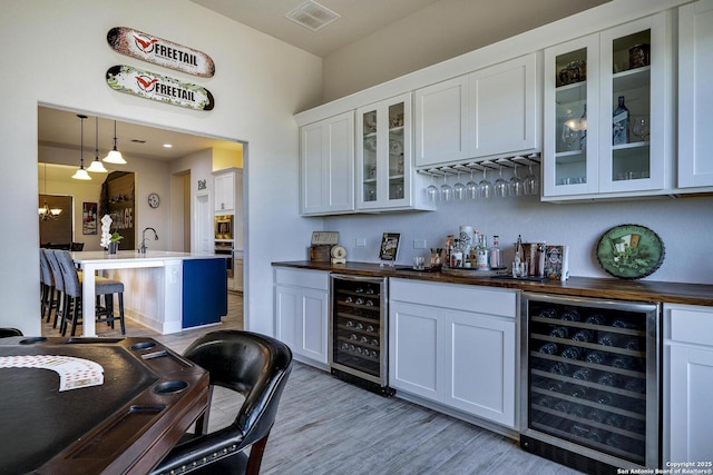 bar with a bar, wine cooler, light wood-style floors, and visible vents