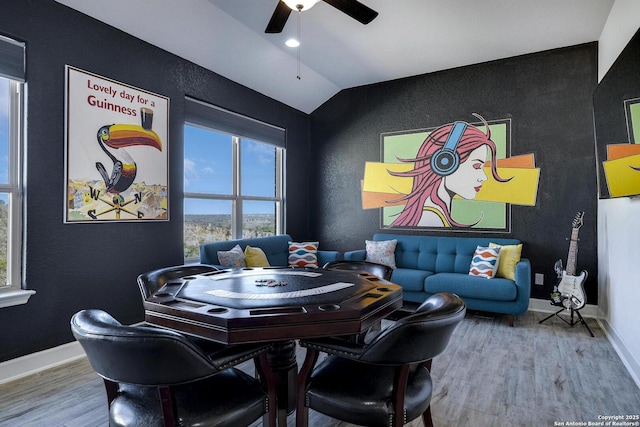 dining room with an accent wall, ceiling fan, baseboards, vaulted ceiling, and wood finished floors