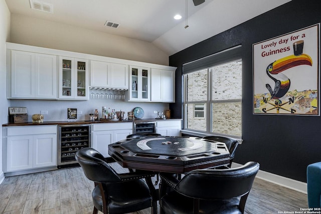 dining room featuring visible vents, beverage cooler, a dry bar, and vaulted ceiling