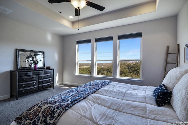 carpeted bedroom featuring a raised ceiling, visible vents, baseboards, and ceiling fan