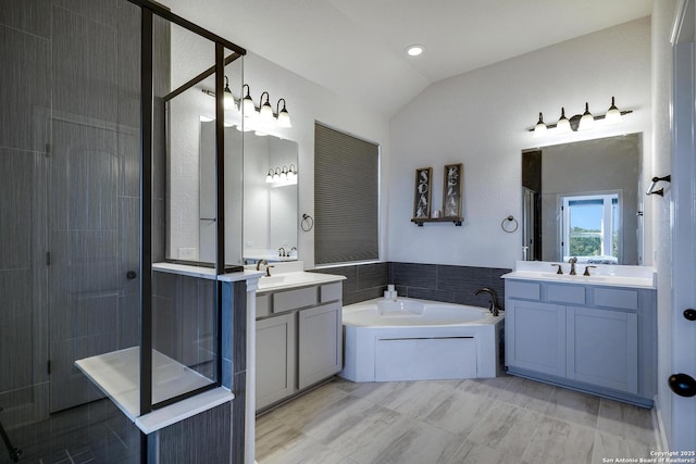 bathroom featuring a shower stall, a garden tub, two vanities, vaulted ceiling, and a sink