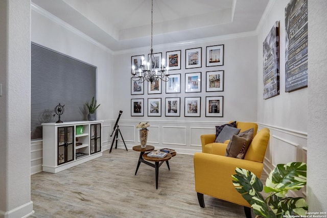 sitting room with a decorative wall, ornamental molding, wood finished floors, a notable chandelier, and a raised ceiling