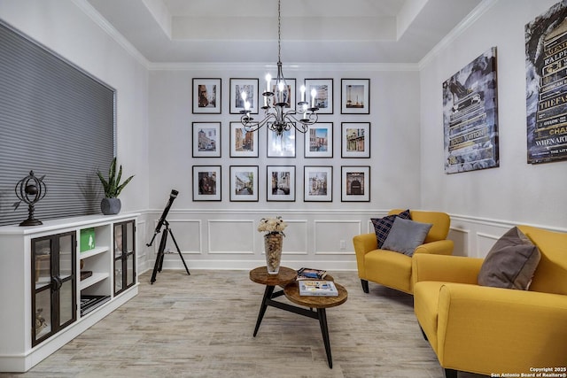 living area featuring a chandelier, a decorative wall, a raised ceiling, and ornamental molding