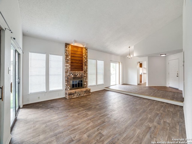 unfurnished living room featuring a notable chandelier, a textured ceiling, wood finished floors, a fireplace, and baseboards