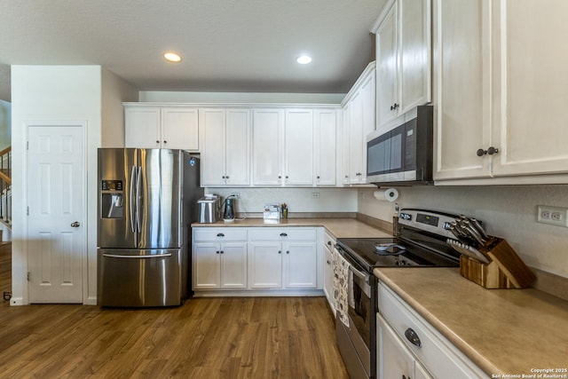 kitchen featuring wood finished floors, recessed lighting, stainless steel appliances, light countertops, and white cabinets