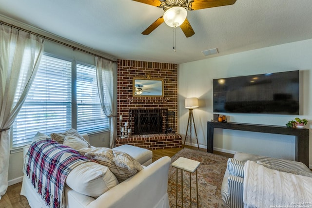 living area featuring wood finished floors, a fireplace, visible vents, and ceiling fan