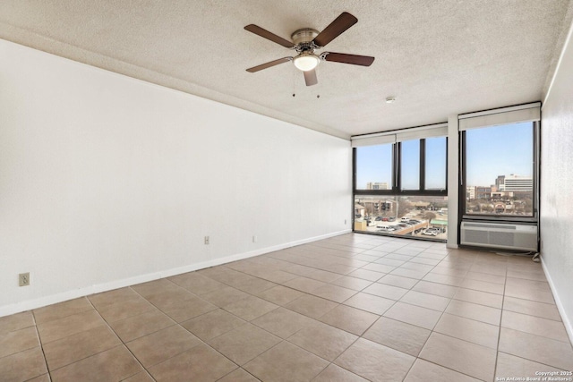 unfurnished room featuring tile patterned flooring, ceiling fan, baseboards, expansive windows, and a textured ceiling