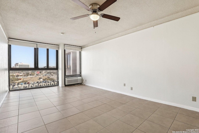 tiled empty room with baseboards, ceiling fan, floor to ceiling windows, a wall mounted air conditioner, and a textured ceiling