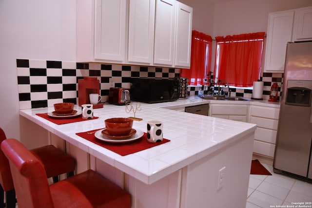 kitchen featuring tile counters, decorative backsplash, stainless steel fridge, white cabinetry, and a sink