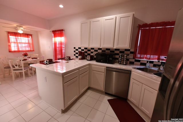 kitchen with a peninsula, a sink, decorative backsplash, light countertops, and stainless steel appliances