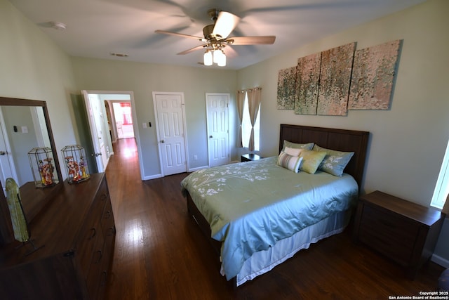 bedroom featuring visible vents, ceiling fan, baseboards, dark wood finished floors, and multiple closets