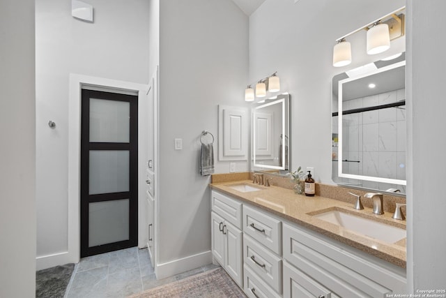 full bathroom with a sink, baseboards, tiled shower, and double vanity