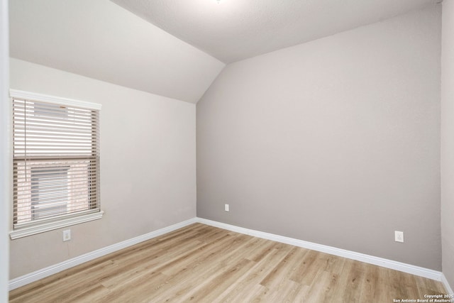 spare room with baseboards, lofted ceiling, and light wood finished floors