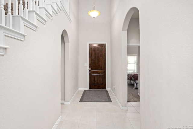 foyer entrance with light tile patterned floors, baseboards, arched walkways, and a towering ceiling