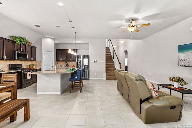 living room featuring visible vents, a ceiling fan, stairway, arched walkways, and light tile patterned flooring