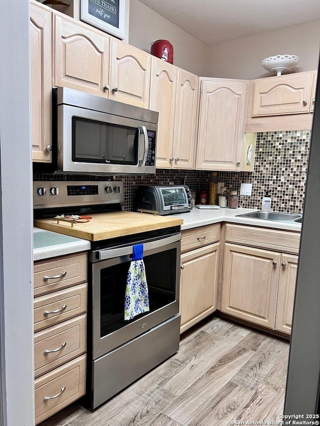 kitchen featuring a toaster, light brown cabinetry, decorative backsplash, light countertops, and appliances with stainless steel finishes