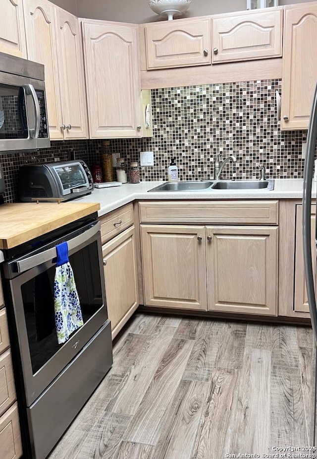 kitchen with light brown cabinets, appliances with stainless steel finishes, tasteful backsplash, and a sink