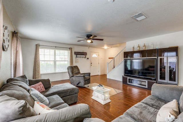 living room featuring visible vents, a textured ceiling, wood finished floors, ceiling fan, and stairs