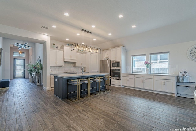 kitchen featuring tasteful backsplash, appliances with stainless steel finishes, white cabinetry, and a kitchen island with sink