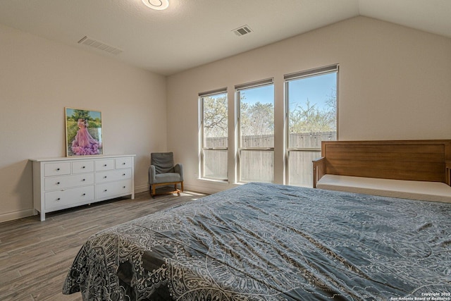 bedroom with visible vents, baseboards, lofted ceiling, and wood finished floors