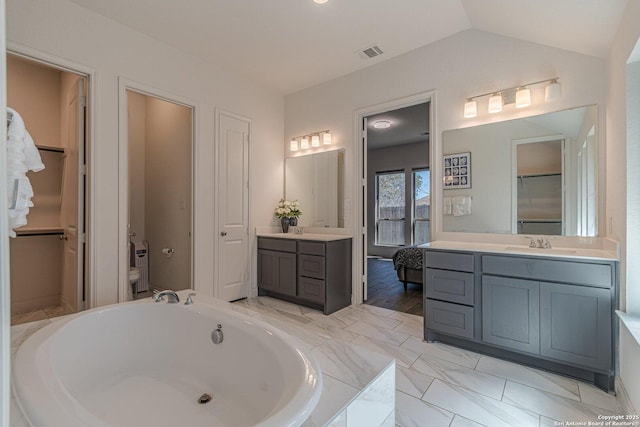 bathroom with visible vents, toilet, vaulted ceiling, a bath, and vanity