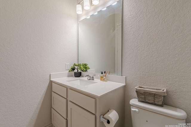 half bath featuring toilet, vanity, and a textured wall