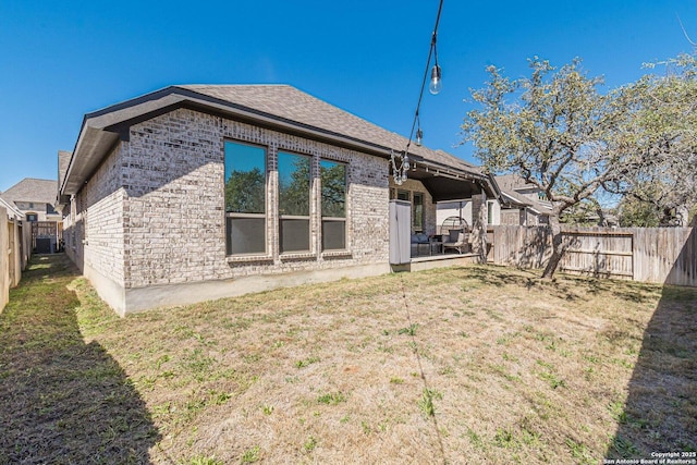 rear view of property featuring a yard, brick siding, a fenced backyard, and a shingled roof