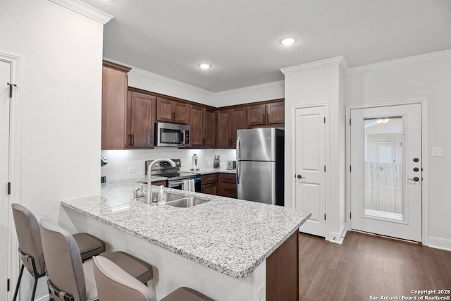 kitchen with wood finished floors, a breakfast bar, a peninsula, a sink, and stainless steel appliances