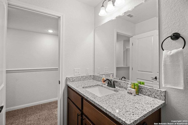 bathroom with vanity, baseboards, visible vents, and a textured wall