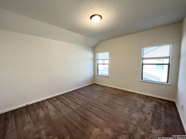 spare room featuring baseboards, dark carpet, and vaulted ceiling