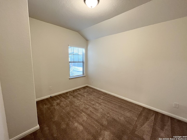 spare room featuring baseboards, lofted ceiling, a textured ceiling, and dark carpet