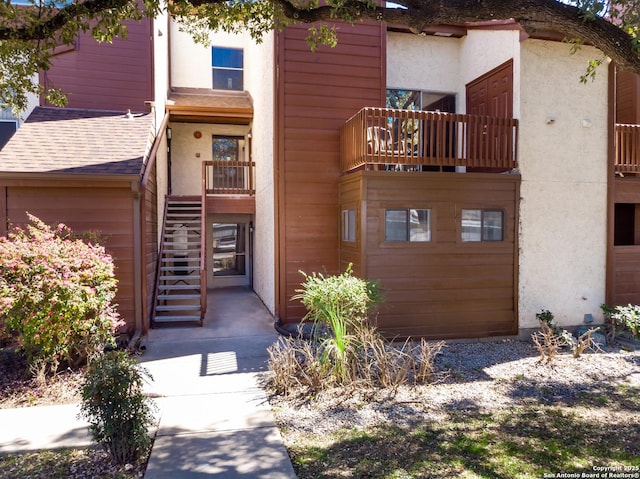 view of front of property featuring stucco siding, roof with shingles, and stairs