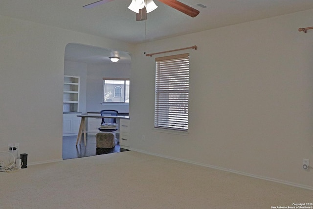 unfurnished office with visible vents, baseboards, carpet, ceiling fan, and arched walkways