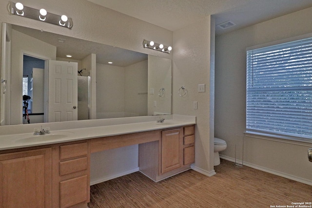 full bathroom with wood finished floors, a shower with shower door, visible vents, double vanity, and a sink