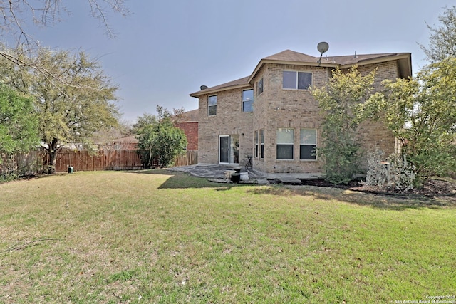 rear view of property with brick siding, a patio area, a lawn, and fence