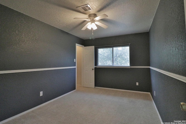 carpeted spare room with visible vents, baseboards, a textured ceiling, and a ceiling fan