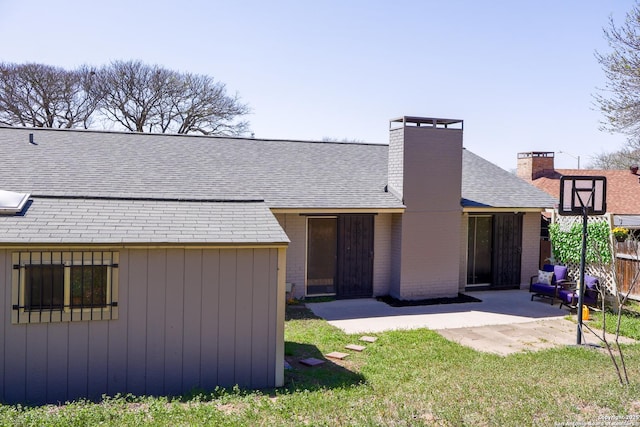 rear view of house with a patio, brick siding, roof with shingles, and a chimney