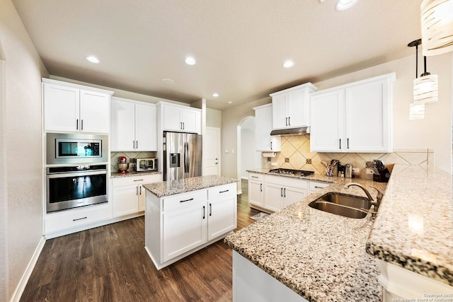 kitchen featuring dark wood-type flooring, a sink, under cabinet range hood, arched walkways, and appliances with stainless steel finishes