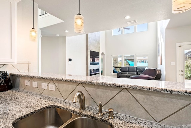 kitchen with light stone countertops, visible vents, a sink, pendant lighting, and tasteful backsplash