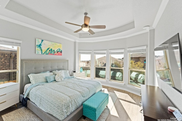 bedroom featuring ceiling fan, a tray ceiling, wood finished floors, and ornamental molding