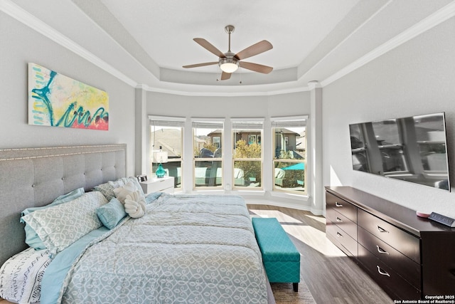 bedroom featuring a ceiling fan, a raised ceiling, wood finished floors, and ornamental molding