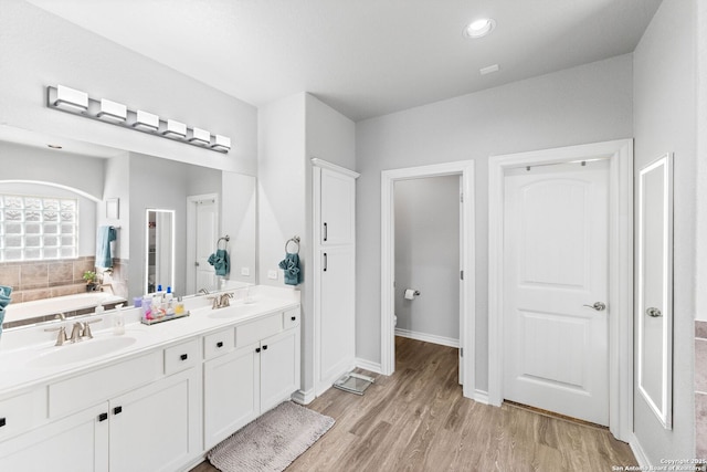 full bath featuring double vanity, wood finished floors, a tub to relax in, and a sink