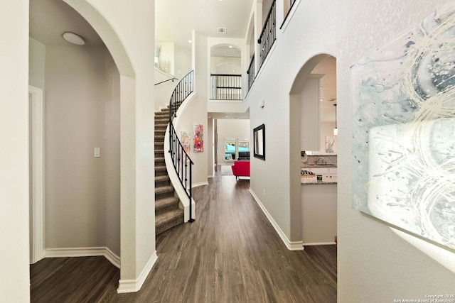 interior space with dark wood finished floors, stairway, baseboards, and a towering ceiling