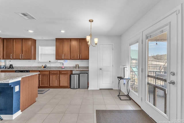 kitchen with light stone counters, light tile patterned floors, brown cabinetry, visible vents, and hanging light fixtures