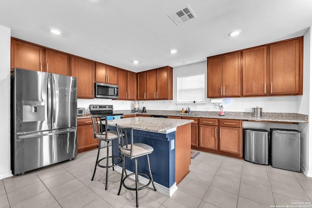 kitchen featuring visible vents, brown cabinets, light stone counters, stainless steel appliances, and a breakfast bar area