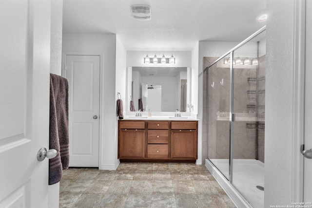 full bathroom featuring visible vents, double vanity, a sink, a shower stall, and a textured ceiling