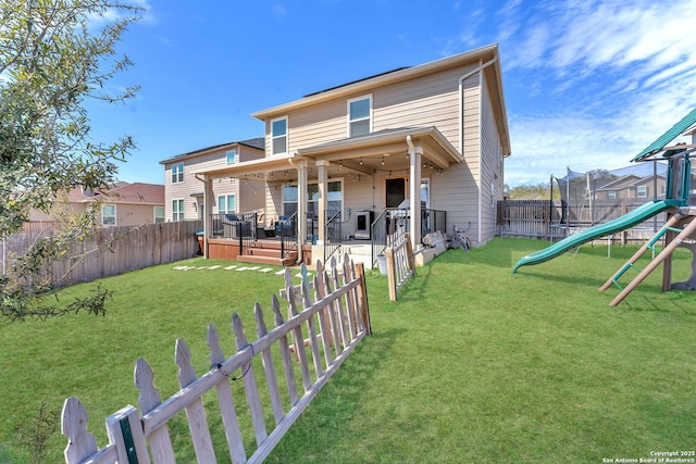 rear view of property featuring a lawn, a trampoline, a fenced backyard, a playground, and a wooden deck